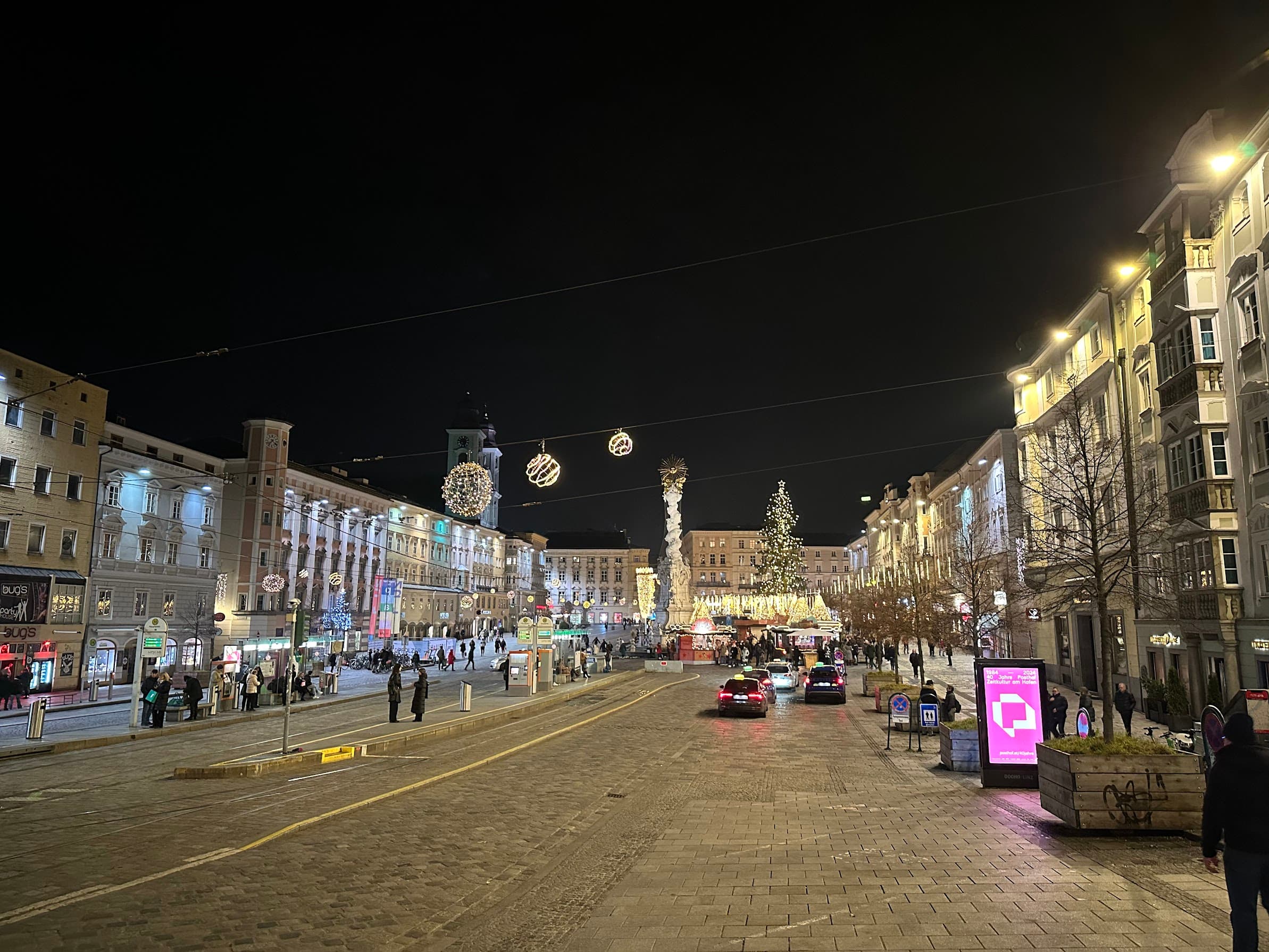 Linz's Hauptplatz at night, decorated for Christmas with market stalls and lights strung over the tram tracks.